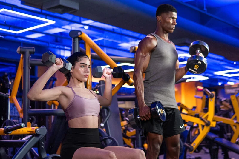 um homem e uma mulher numa academia fazendo exercício de levantamento de peso